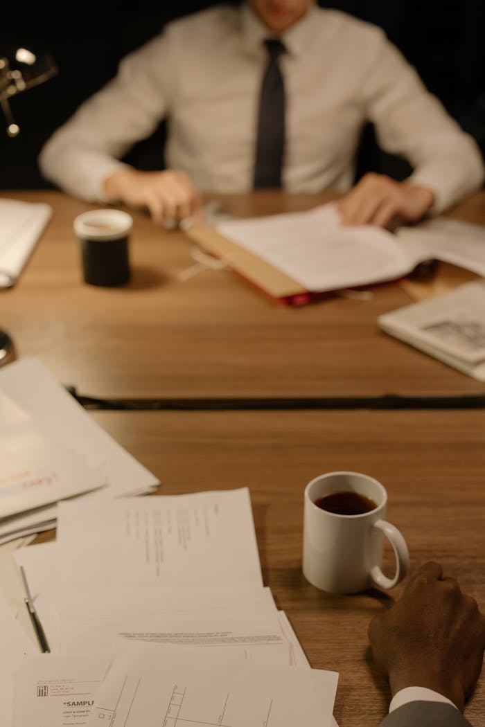 A business setting with coffee cups, documents, and hands on a wooden table.