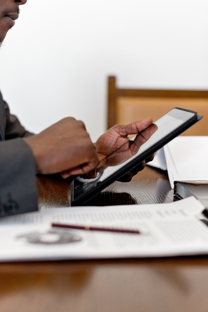 Professional adult using a digital tablet in an office setting with documents.